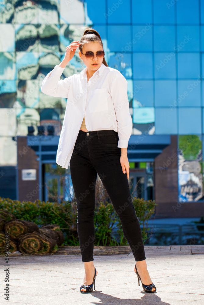 Fototapeta premium Portrait of a young brunette woman in black jeans and white shirt