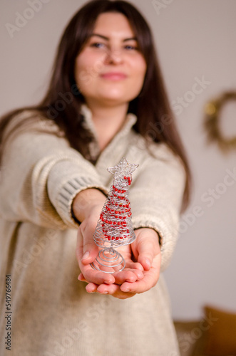 Young caucasian smiling woman blurred, holding small metallic Christmas tree in focus, in room with decorations and bed