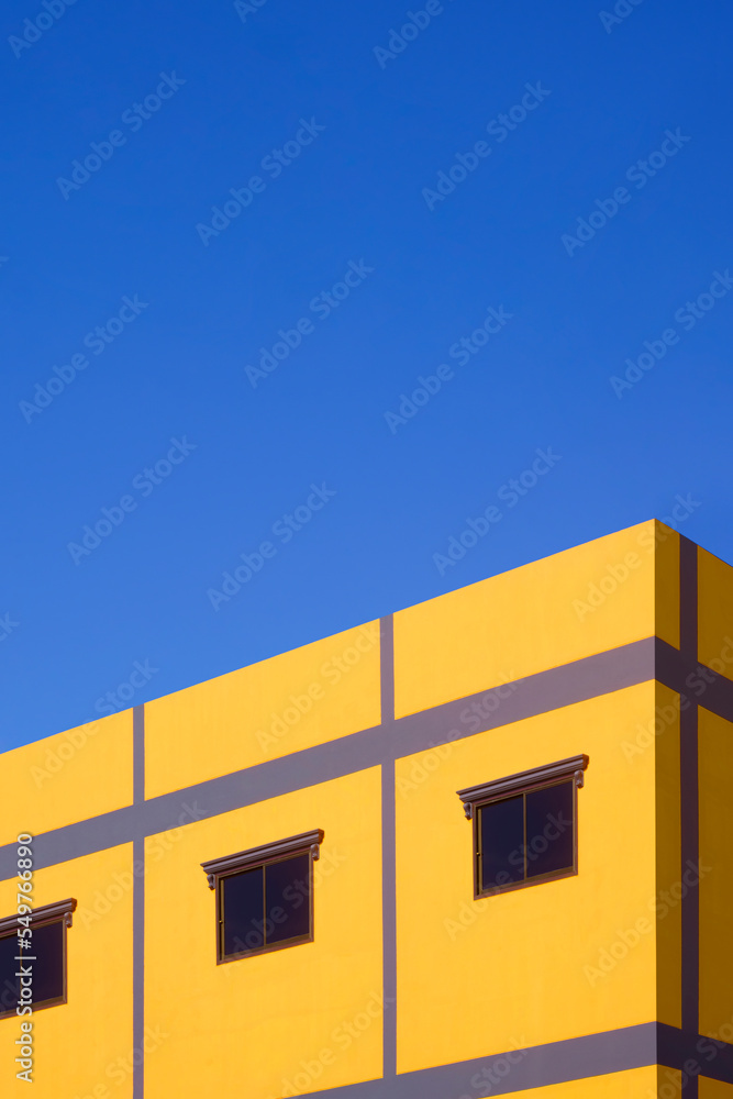 Street minimal exterior architecture background. Glass windows on colorful yellow and purple house building wall against blue clear sky background in vertical frame Street minimal exterior architecture background. Glass windows on colorful yellow and purple house building wall against blue clear sky background in vertical frame