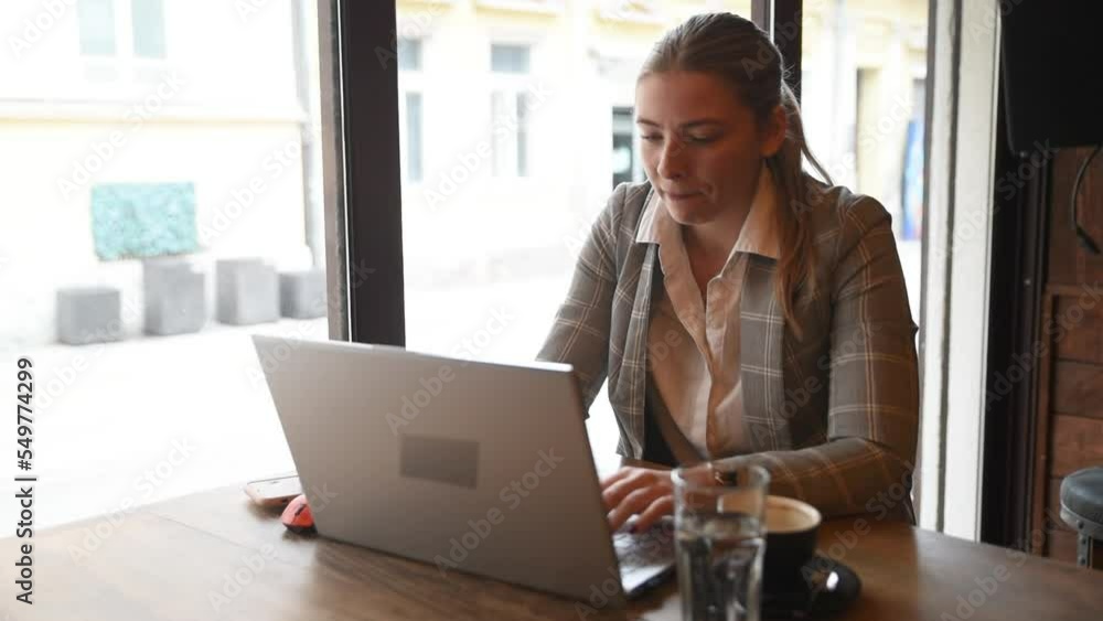 Young business woman sitting in the coffee shop during the lunch break drinking coffee and work on the laptop computer. Freelancer business person working on the new project for foreign company. Young business woman sitting in the coffee shop during the lunch break drinking coffee and work on the laptop computer. Freelancer business person working on the new project for foreign company.