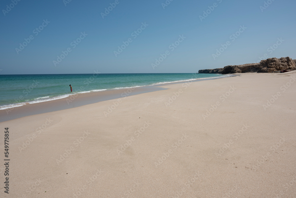 Woman alone at a wild Beach of Ras Al Jinz and going to swim in the ocean, Sultanate of Oman. 