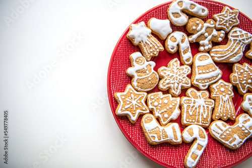 Christmas homemade gingerbread cookies of different shapes decorated with white icing laying on red plate on white background. Festive flatlay
