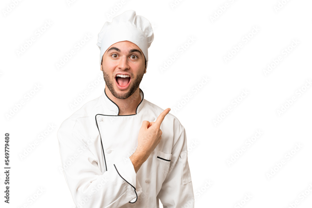 Young handsome chef man over isolated background surprised and pointing side Young handsome chef man over isolated background surprised and pointing side
