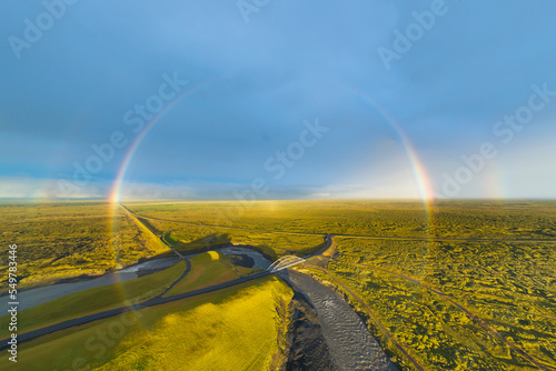 Aerial view of full rainbow over landscape with road and bridge, south Iceland