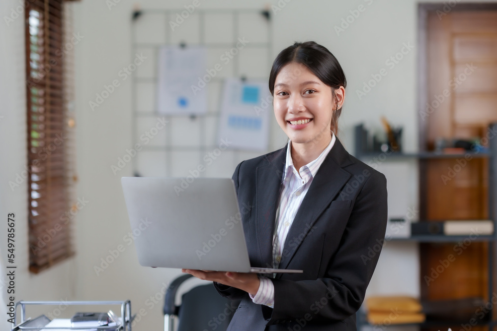 Beautiful Asian business woman standing holding a laptop in the office Beautiful Asian business woman standing holding a laptop in the office