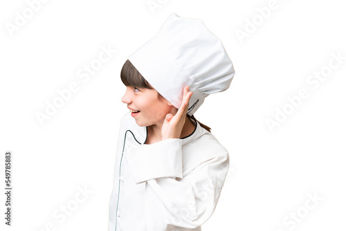 Little caucasian chef girl over isolated background listening to something by putting hand on the ear