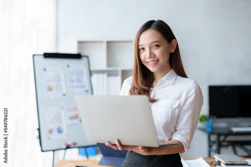 Beautiful Asian business woman standing holding a laptop in the office Beautiful Asian business woman standing holding a laptop in the office