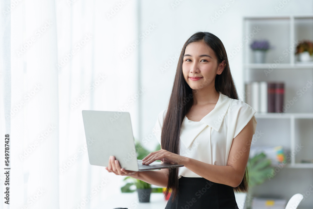 Beautiful Asian business woman standing holding a laptop in the office Beautiful Asian business woman standing holding a laptop in the office