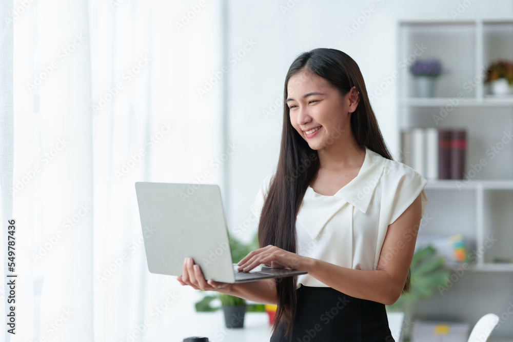 Beautiful Asian business woman standing holding a laptop in the office Beautiful Asian business woman standing holding a laptop in the office