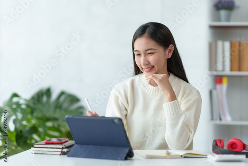 Attractive Asian business woman sitting at work happily working using tablet at office and smiling comfortably.