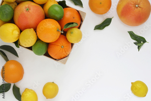 Citrus fruits frame or border on white background. Top view. Arranged oranges, lemons, grapefruits and limes with leaves, whole, scattered and in box. Copy space. Photo from above.