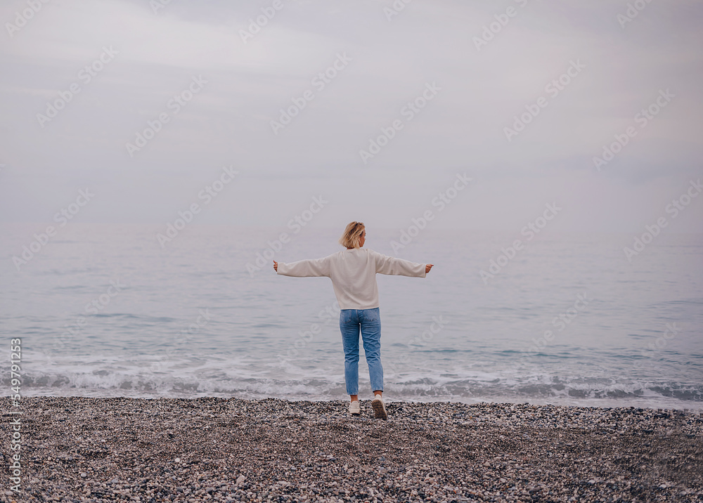 happy woman stands on the sea sand and shows her hand in the sky. the subject is blurred