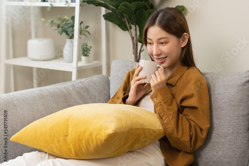 Modern air humidifier during relaxed, rest on sofa, happy asian young woman, girl enjoying, drinking with aromatherapy steam scent from essential oil diffuser comfortable in living room at home.