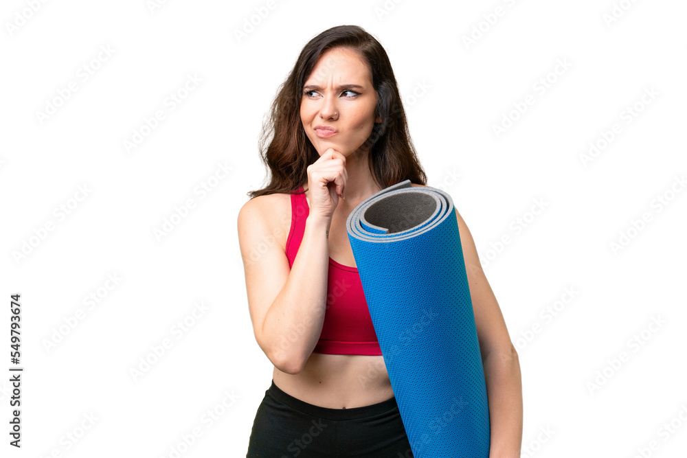 Young sport woman going to yoga classes while holding a mat over isolated background having doubts and thinking Young sport woman going to yoga classes while holding a mat over isolated background having doubts and thinking