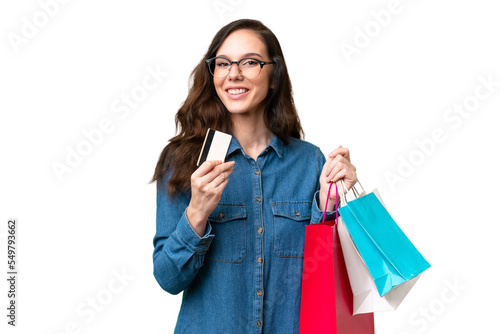 Young caucasian woman over isolated background holding shopping bags and a credit card