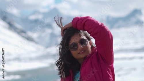 Portrait of tourist Indian girl tourist with sunglasses looking at snow covered mountains at Shinku La Pass, India. Travel lifestyle. Female travel influencer enjoying vacation in mountains photo