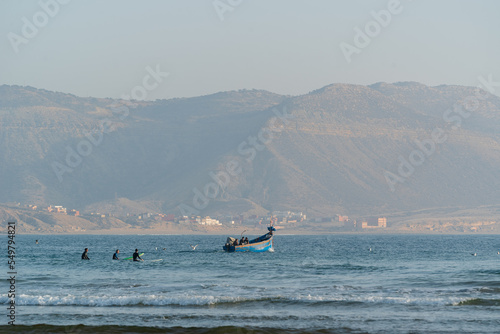 A group of surfers at the line-up and a Moroccon wooden fishing boat at Imsouane, Morocco photo