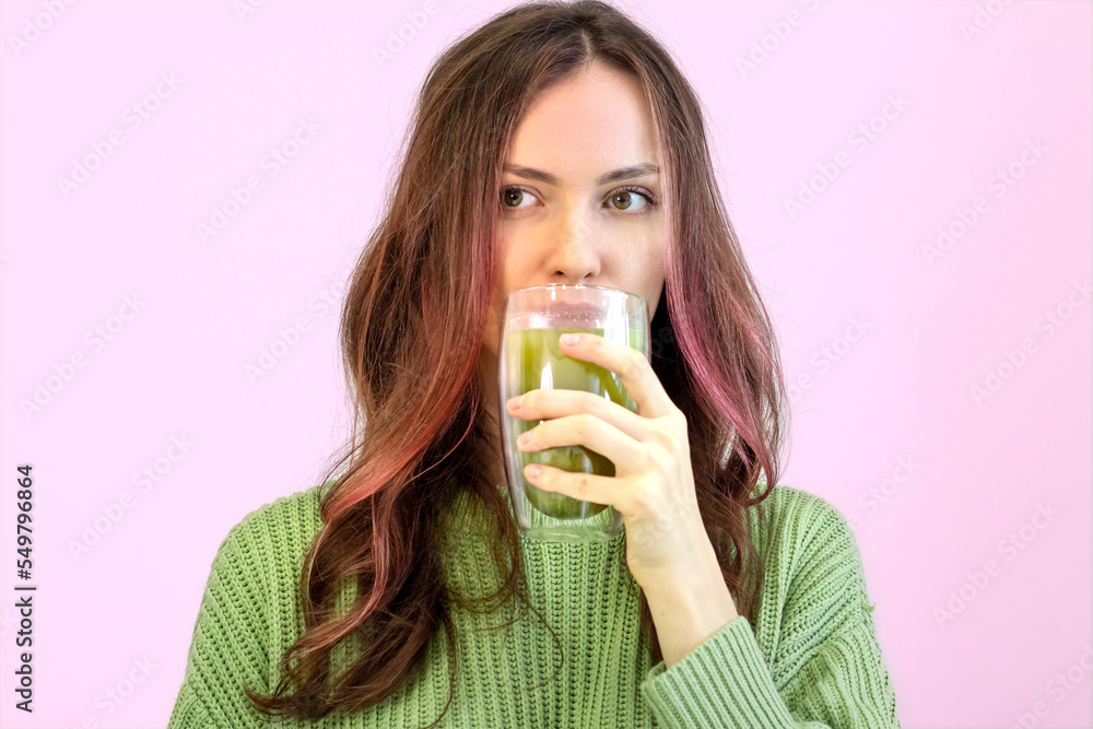 Beautiful woman with curly hair with fashionable hair is drinking matcha green tea on a pink background. Beautiful woman with curly hair with fashionable hair is drinking matcha green tea on a pink background.