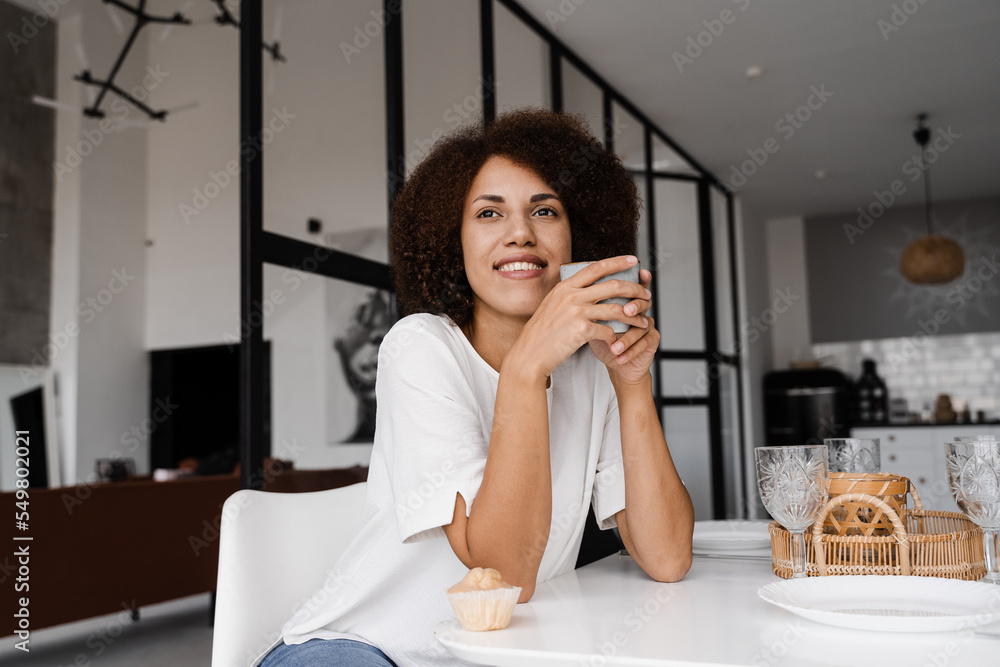 Attractive african woman with coffee and cake sitting at the dinner table. Cozy morning of african american girl on the kitchen at home. Attractive african woman with coffee and cake sitting at the dinner table. Cozy morning of african american girl on the kitchen at home.