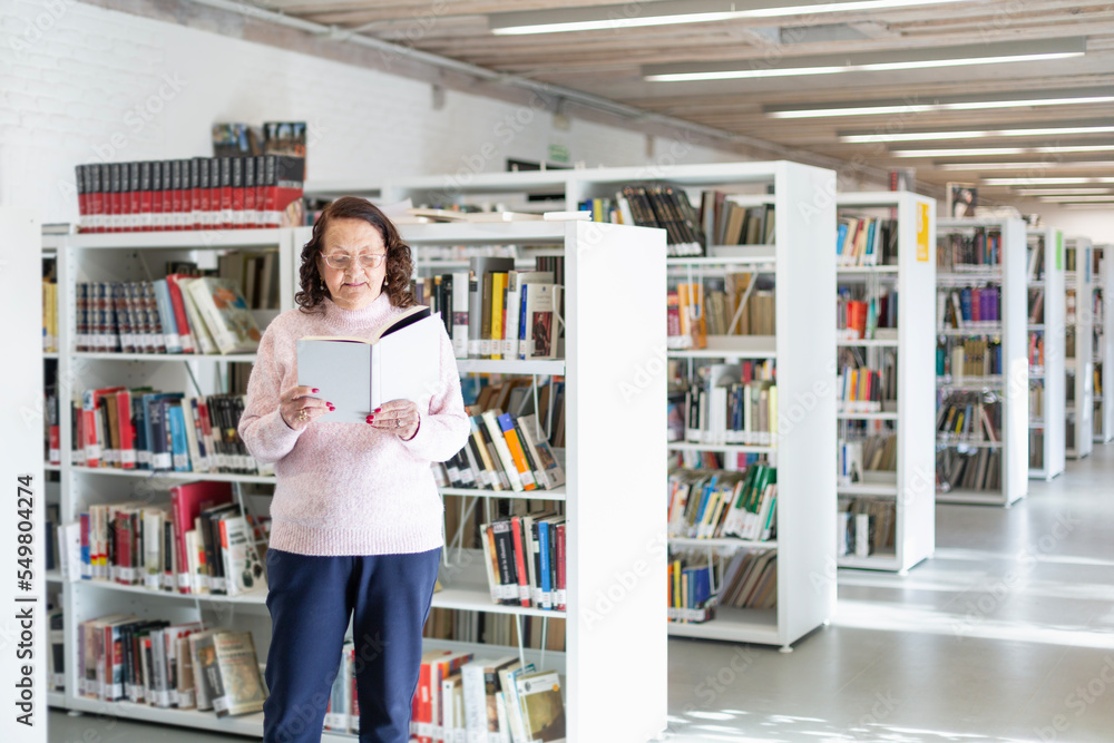 Elderly person reading a book in a public library. Space for text. Elderly person reading a book in a public library. Space for text.