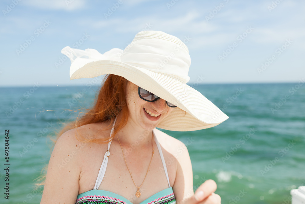 young red-haired girl in a hat on the background of the sea