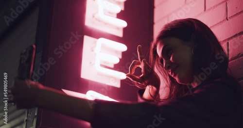 Phone, selfie and woman on a street at night in city with neon lights outside party or club. Happy, peace sign and girl taking a picture on smartphone outdoor in the road of an urban town in New York
