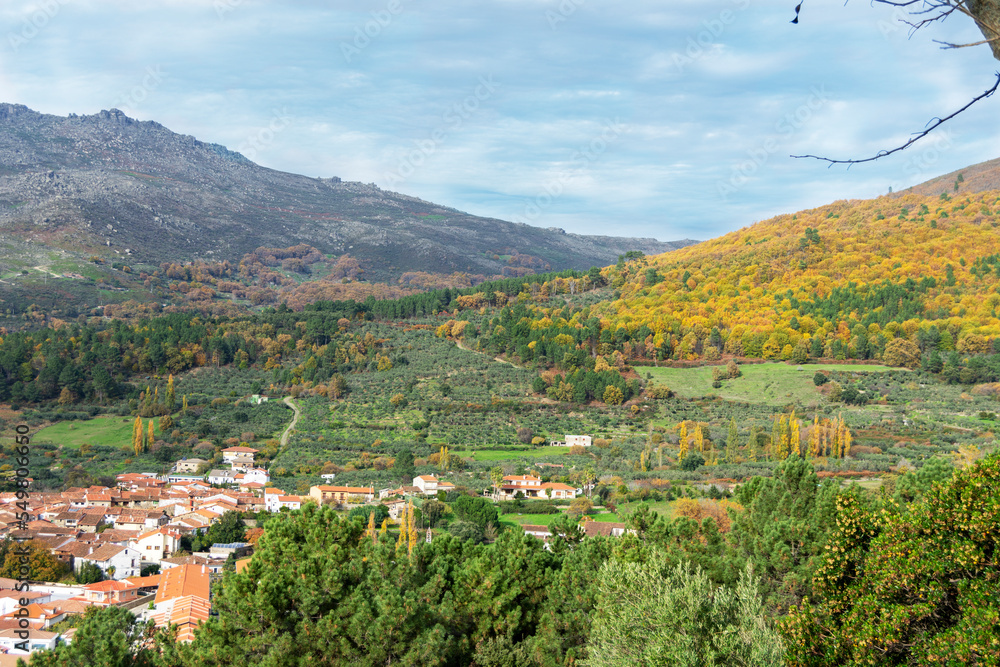 Paisaje de un pueblo montañoso español en otoño. Arboles en tonos naranjas y casas con paredes blancas 