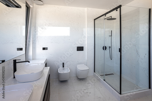 white marble bathroom with window  shower  toilet  bidet and sinks