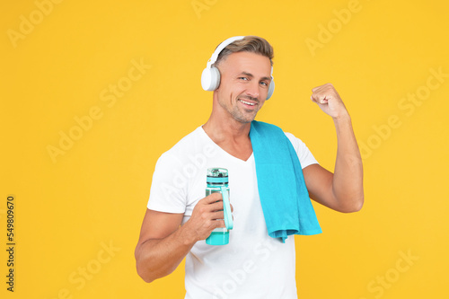 glad fitness man with towel and bottle after training. fitness man in headphones hold sport bottle.