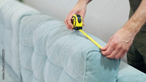person uses a building meter to measure a sofa, moving house, choosing a sofa in a store. Home improvement sofa size measure ruler tool. Man measuring sofa, closeup. Construction tool
