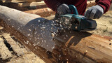 Worker grinds a log with an electric tool. Preparation for building a house.