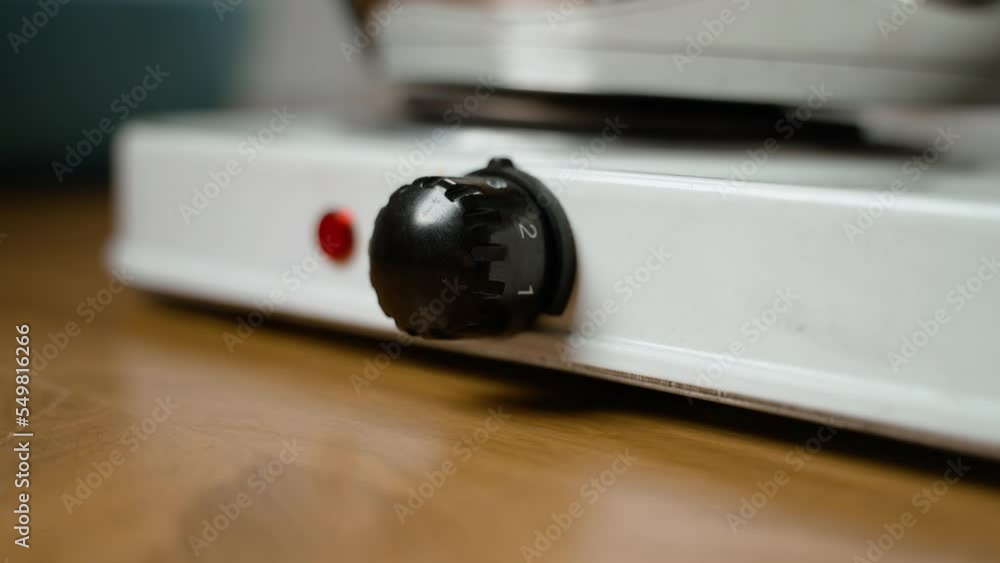 Kitchen devices. Person turns button of electric stove and adjusts temperature mode. Woman turns on electric stove. Wheel with numbers that regulate temperature. Kitchen equipment. Cooking. Close-up Kitchen devices. Person turns button of electric stove and adjusts temperature mode. Woman turns on electric stove. Wheel with numbers that regulate temperature. Kitchen equipment. Cooking. Close-up