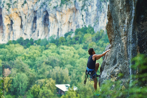 Man climber climbs on a rocky wall with beautiful mountains view on background, making hard wide move and gripping hold