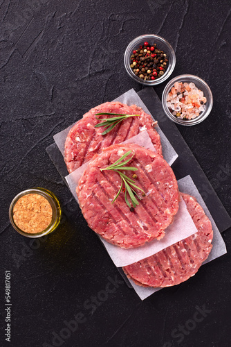 Raw fresh hamburger patties or cutlet ready to cook on black textured background. Minced beef steak burgers with spices. Top view.