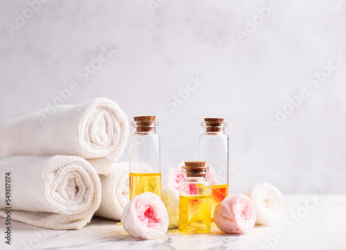 Spa setting. Bottles with rose essential aroma oil, rose flowers  and white towels on light  grey textured background. Selective focus. Place for text.