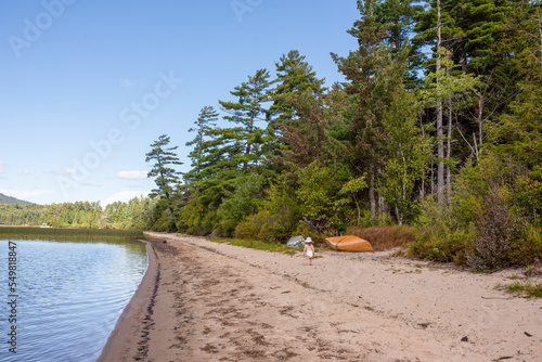 A toddler walks near a couple of kayaks along the beach on Middle Saranac Lake in New York