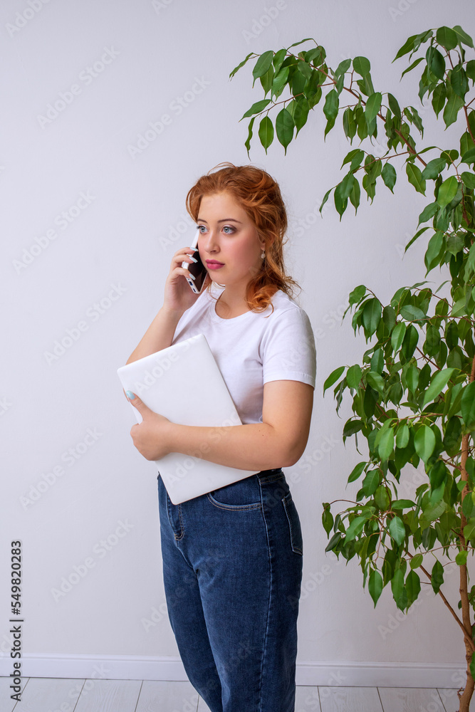 Office worker talking on the phone indoors. The girl is holding a laptop. Vertical photo of people. Office worker talking on the phone indoors. The girl is holding a laptop. Vertical photo of people.