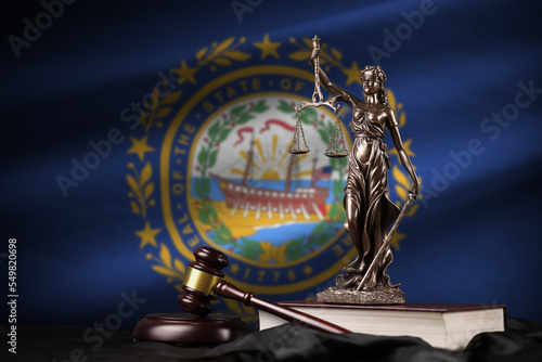 New Hampshire US state flag with statue of lady justice, constitution and judge hammer on black drapery. Concept of judgement and guilt photo