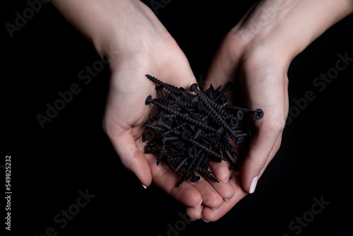 Woman's hands holding screws and dowels in palms. Isolated on black. female hands hold screws nails washers nuts on a black background