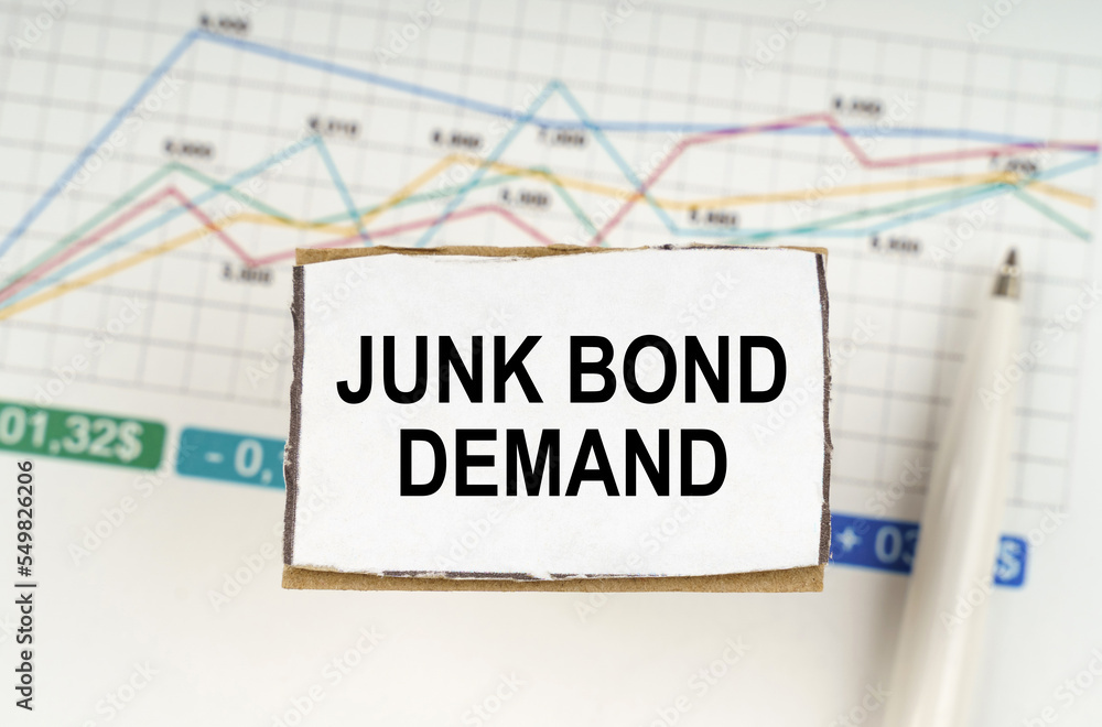 Against the background of business graphics and pens, a sign with the inscription - JUNK BOND DEMAND Against the background of business graphics and pens, a sign with the inscription - JUNK BOND DEMAND
