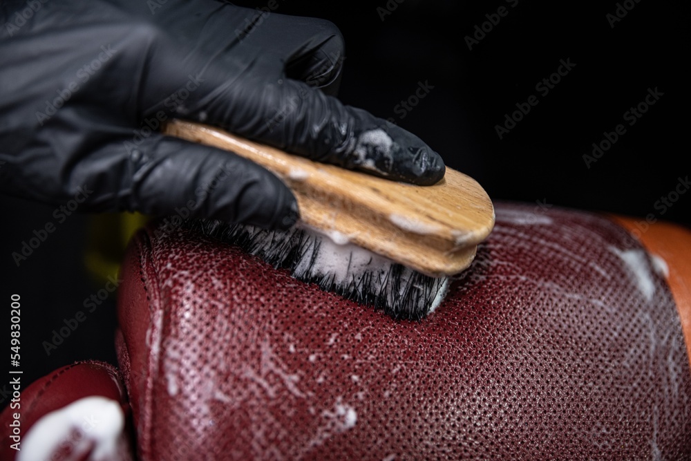 employee of a car wash or a car detailing studio washes the leather upholstery of the car with a brush