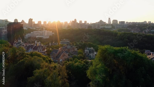 Aerial view of cityscape with bright evening sunlight. Many trees and buildings.