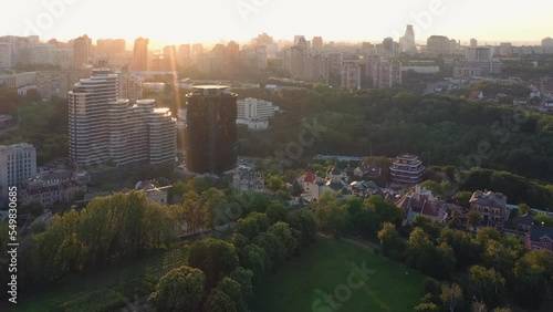 View from drone on the city with bright evening sunlight. Green trees and buildings.