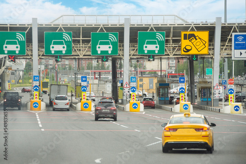 View with cars at the entrance or exit to a toll road limited by a barrier. Cashless payment transponder barrier, speed limit signs.