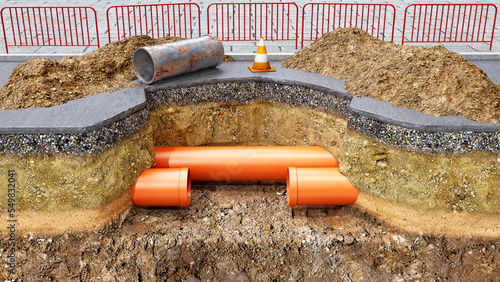 Concept of road works and underground pipes renovation, new orange pvc pipes are installed instead of old rusty section, slice of ground and a pit digged in the asphalt, mounds of soil are upside 