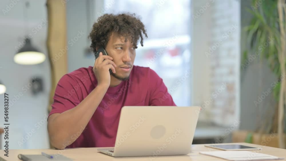 Displeased African Man Talking Angrily on Smartphone at Work Displeased African Man Talking Angrily on Smartphone at Work