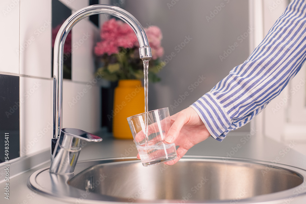 Woman pouring a glass of water from tap in the kitchen sink. Filling up