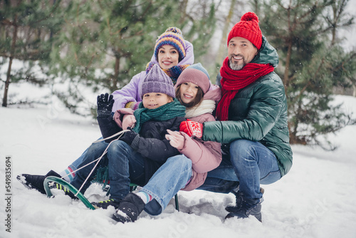 Photo of positive cheerful little child wife husband dressed coats riding sledges together outdoors urban forest park