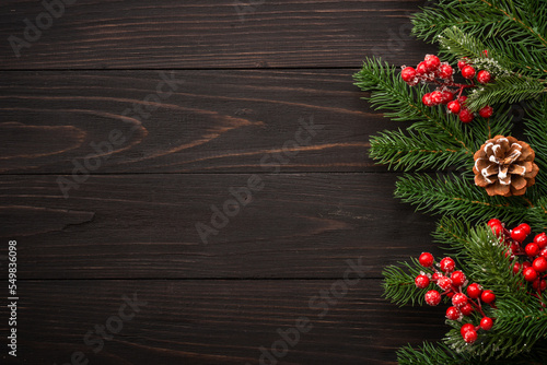 Christmas greeting card. Fir tree brunch and red decorations on wooden background. flat lay with copy space.