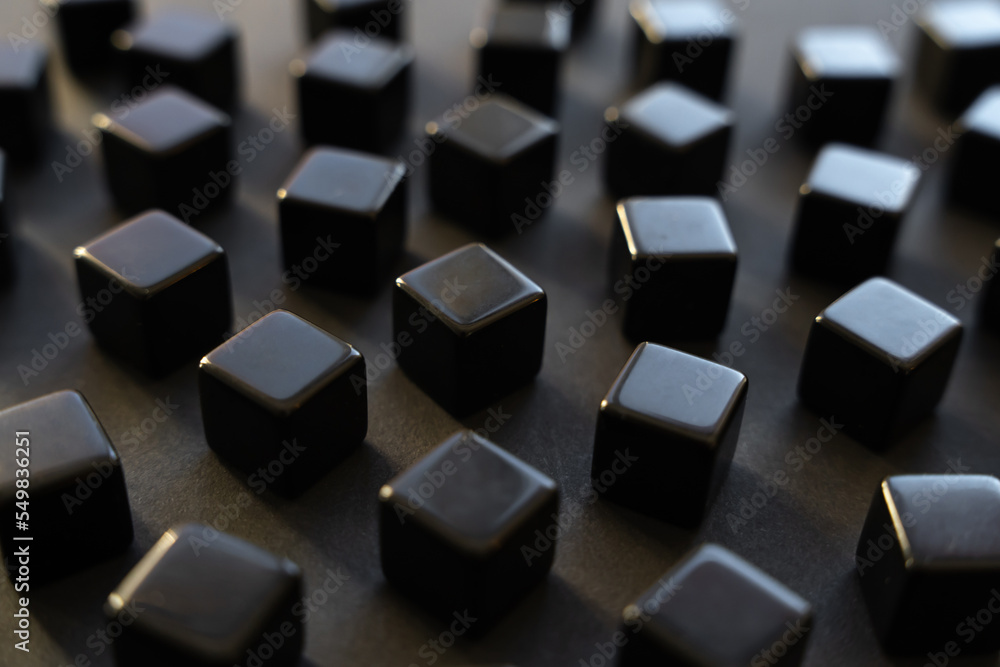 Black blocks on a dark background. Scattered cubes. Abstraction, field blur. Simplicity and elegance. Solidity, shine. Black blocks on a dark background. Scattered cubes. Abstraction, field blur. Simplicity and elegance. Solidity, shine.